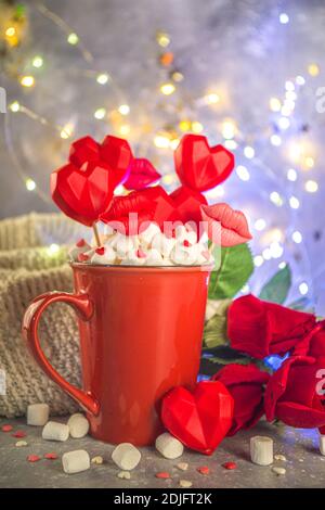 Valentine`s Day Süßwaren-Konzept, festliche Feiertagshintergrund mit heißer Schokolade rote Tasse und Set von roten Herzen Süßigkeiten auf Sticks in Tasse, mit roten Rosen und Stockfoto